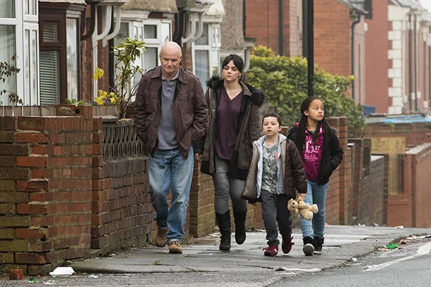A scene from I, Daniel Blake showing Daniel and the family he befriends walking down the road